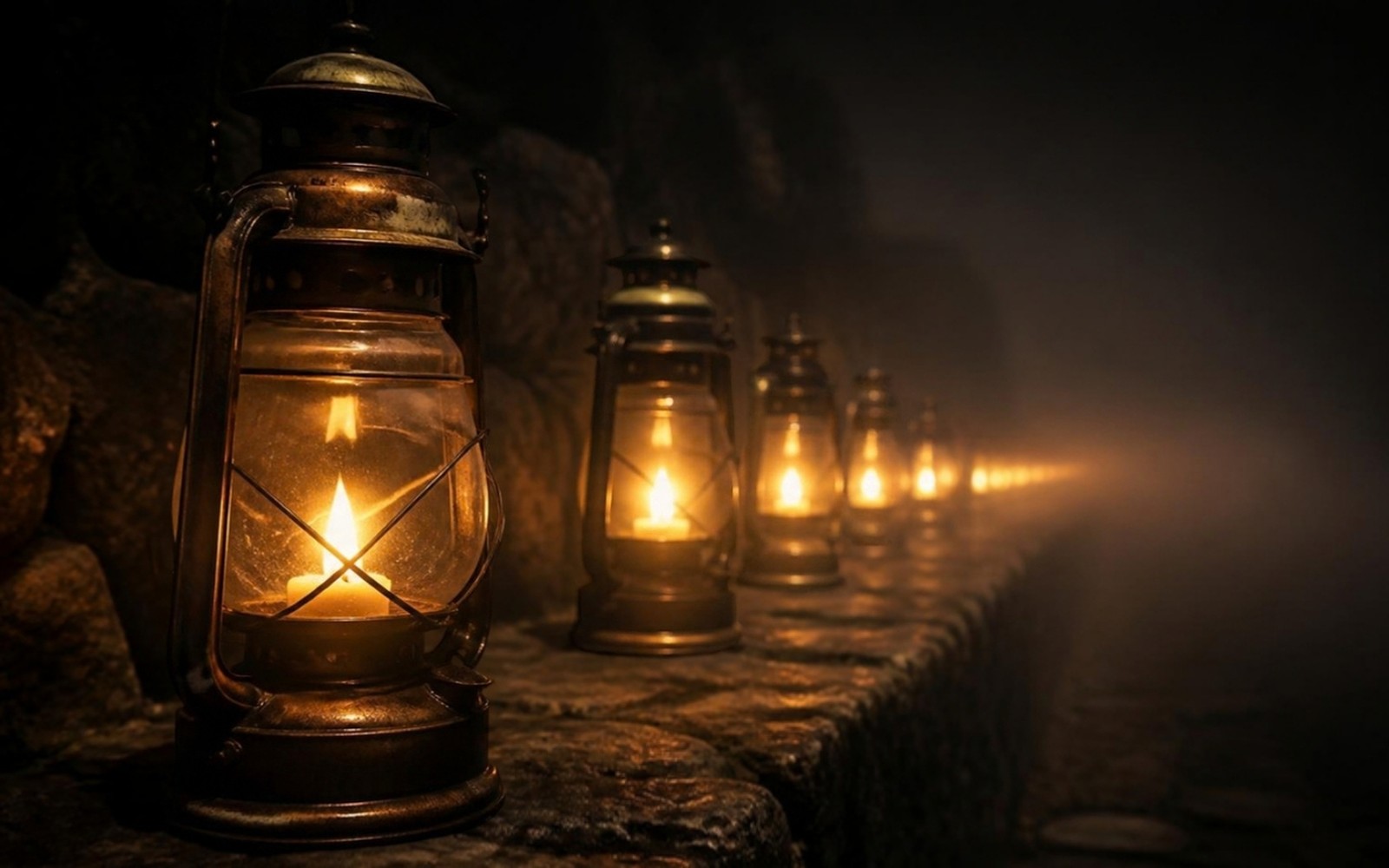 A row of old brass lanterns, each lit with warm amber flame, receding into dense fog on a dark stone path at night