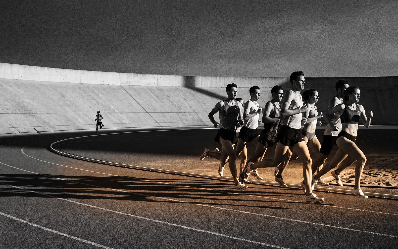 A row of ten runners crossing a finish line together except for one far behind, long shadows, dusk