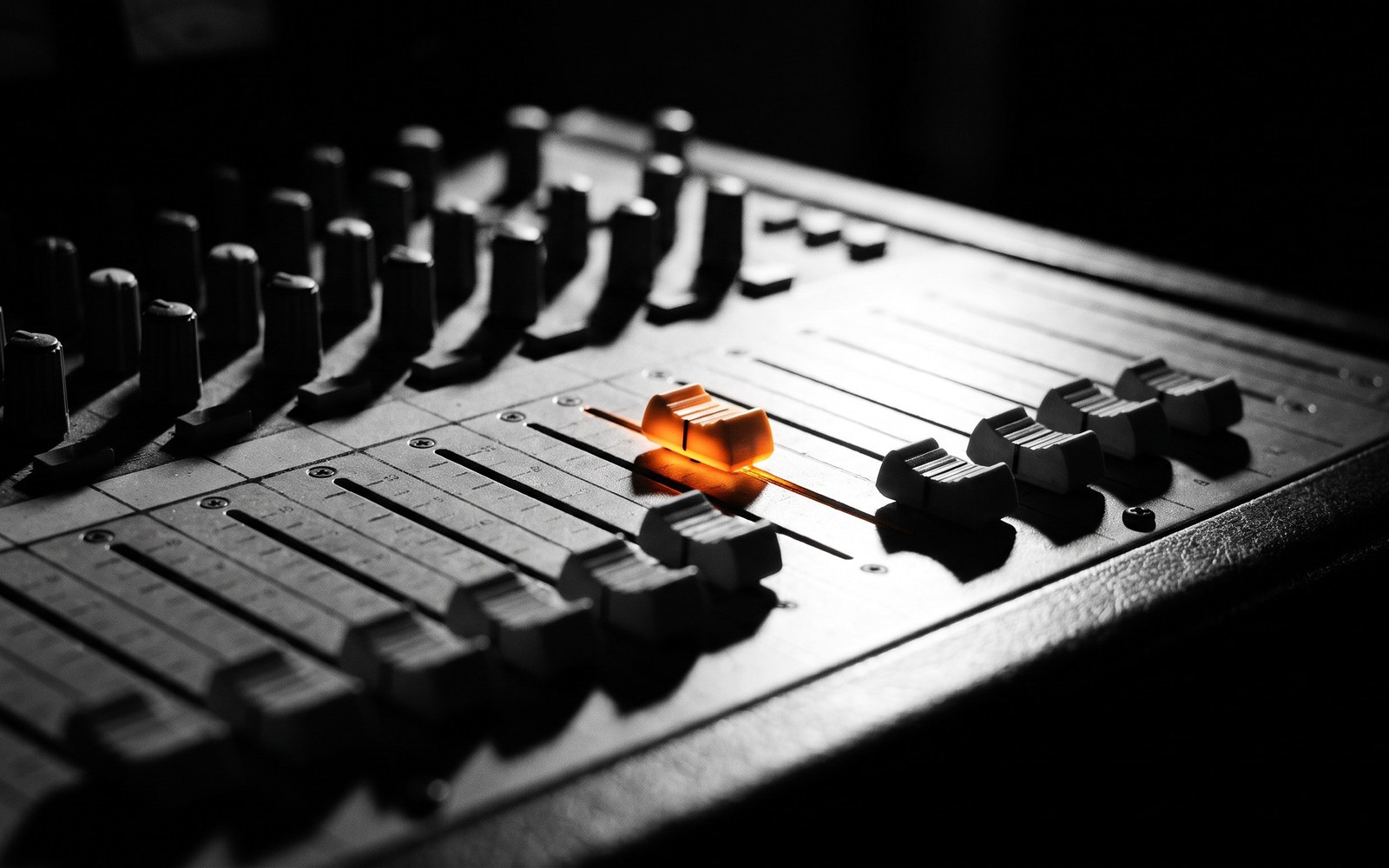 A vintage analog mixing console with a row of faders pushed down low except one glowing fader pushed up high