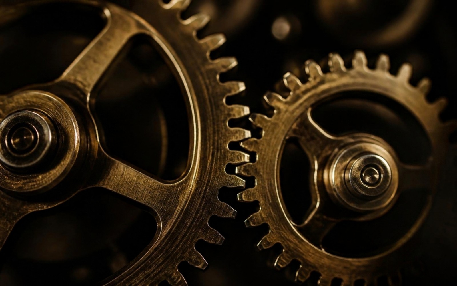 Two interlocked brass gears, lit warmly against a dark background, teeth meshed together mid-turn