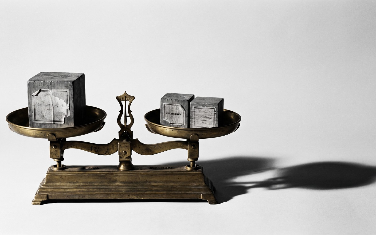 An old-fashioned balance scale, one side holding a single labeled block, the other side holding two smaller labeled blocks in even balance