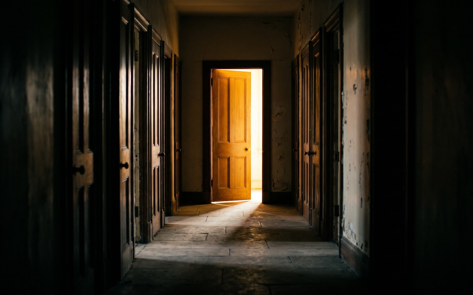 A single warmly lit open door glowing at the end of a long hallway, other doors fading into shadow on either side