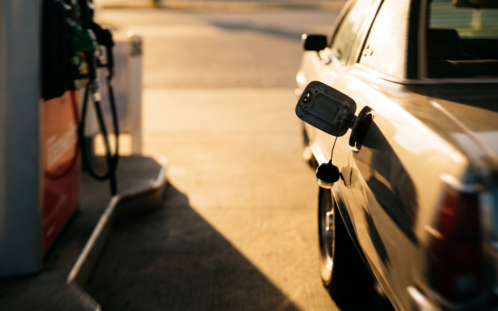 A car driving away from a gas station at golden hour with the fuel cap door left open and the cap dangling