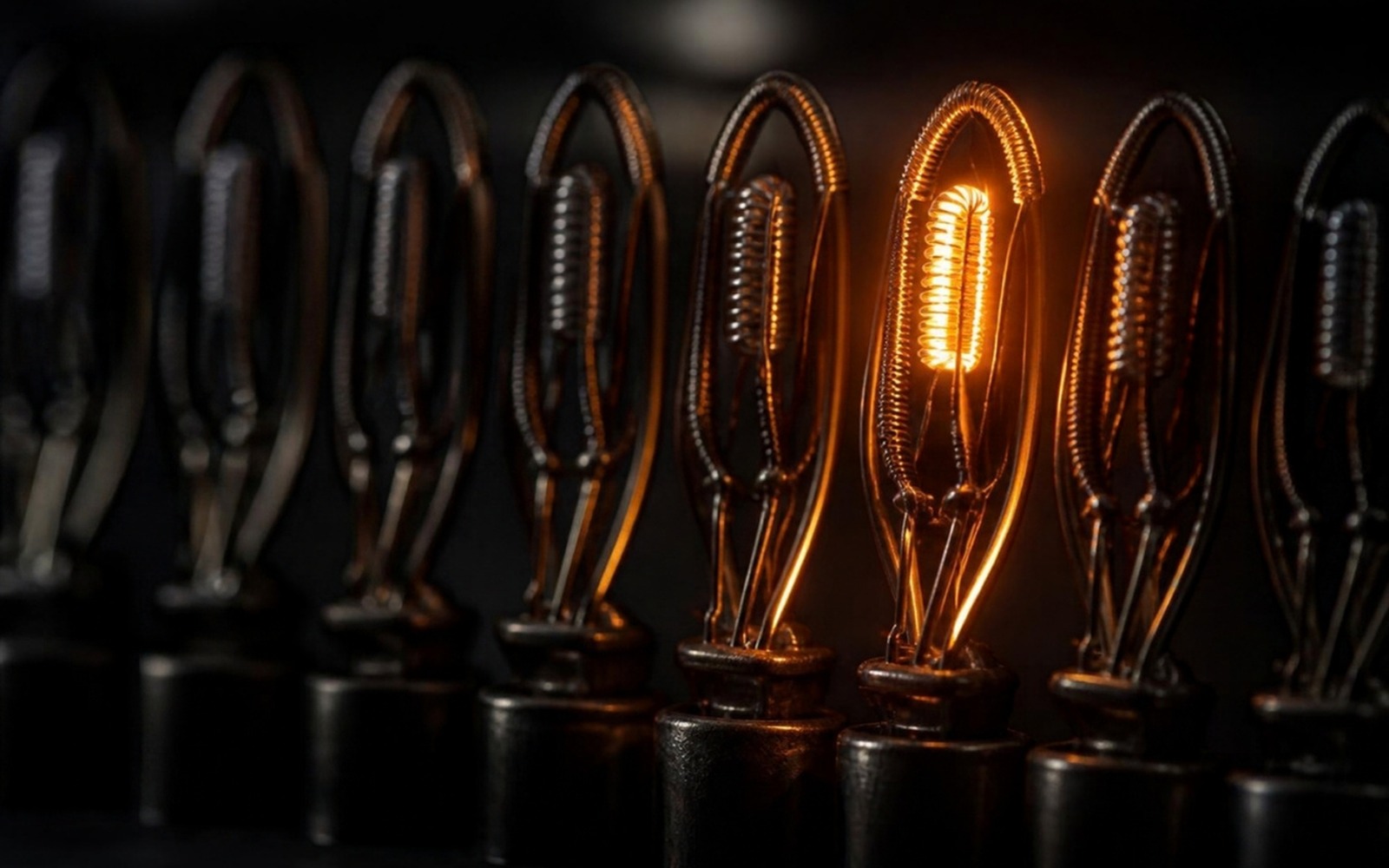 Macro photograph of a row of dark, unlit vacuum-tube filaments with exactly one filament glowing warm amber