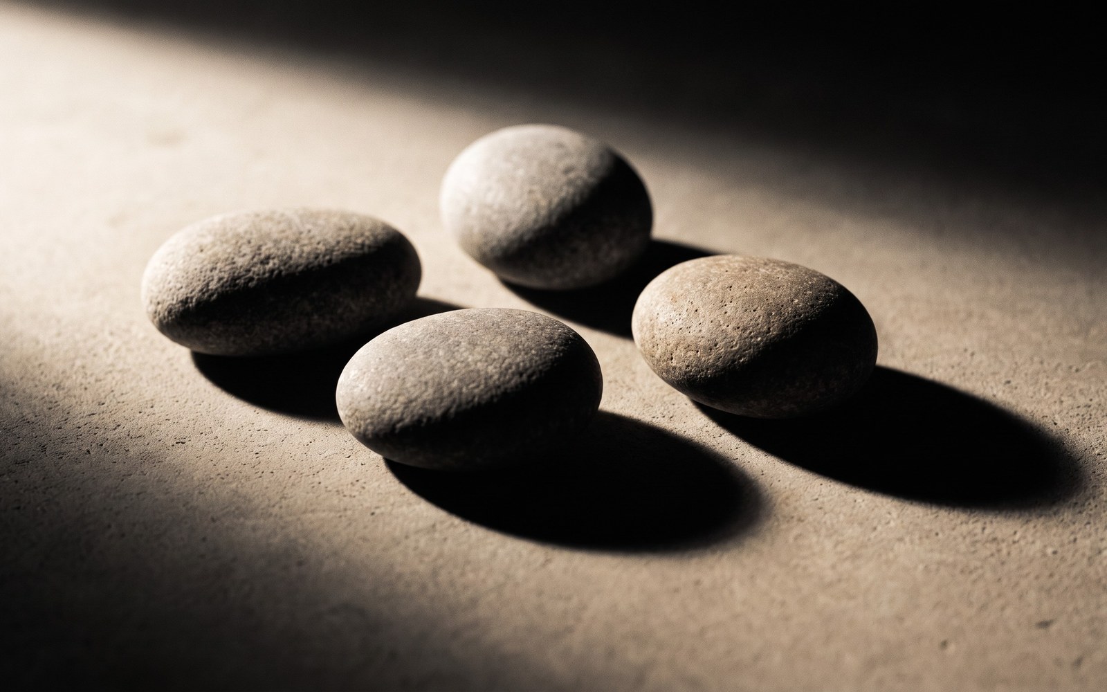 Four smooth stones arranged loosely on a plain surface in soft directional light
