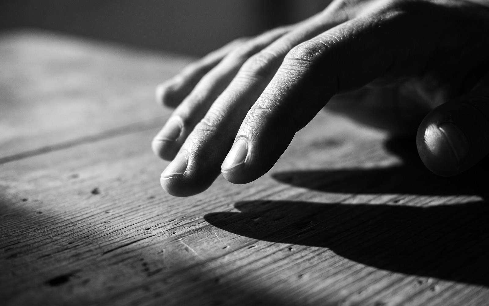 Fingertips drumming on a bare wooden table, warm side lighting and long shadows
