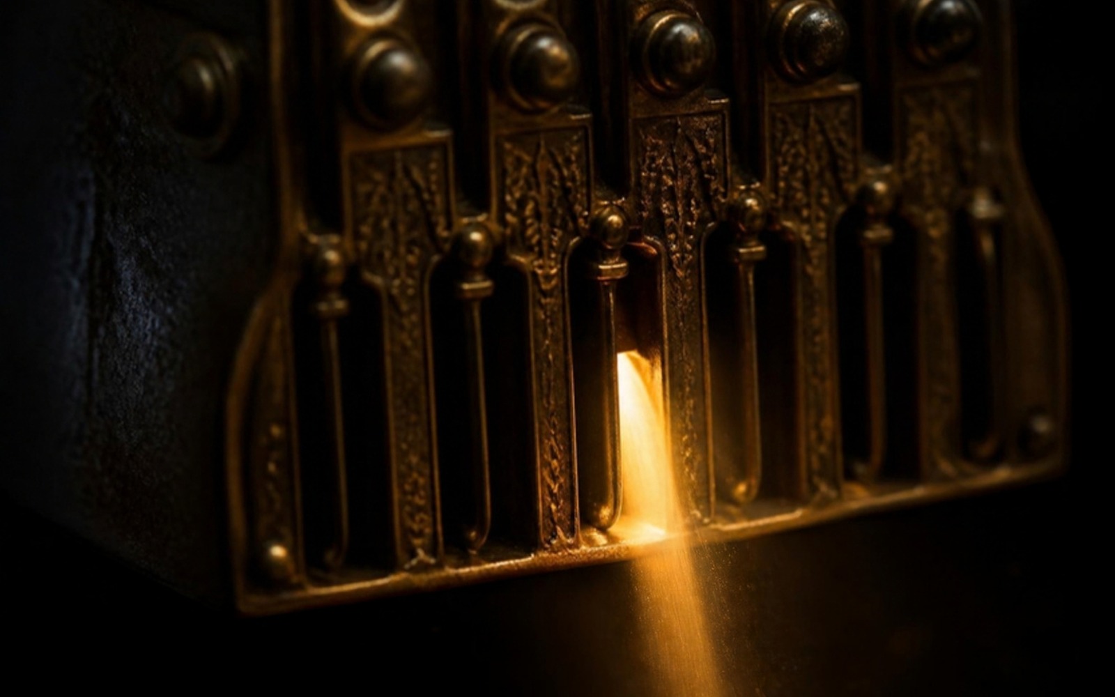 Macro photograph of an ornate brass mechanism with several closed dark channels and one narrow channel glowing with warm amber light