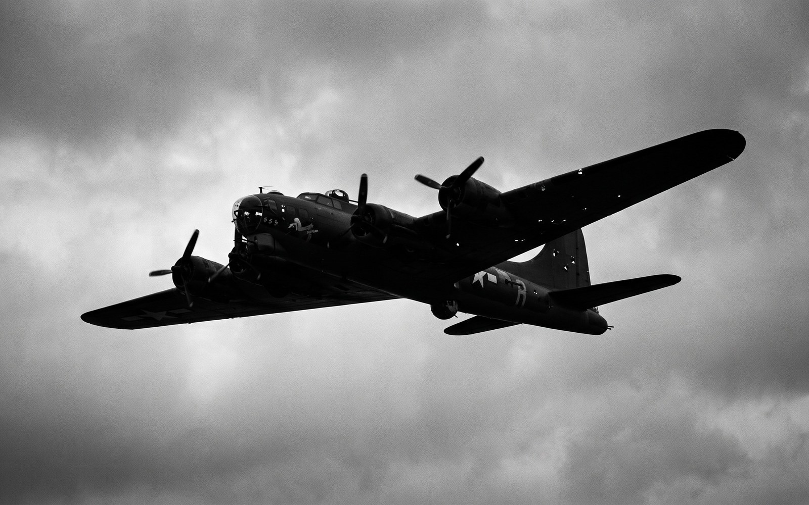 A WWII-era propeller bomber silhouetted against a cloudy sky, in muted black and white