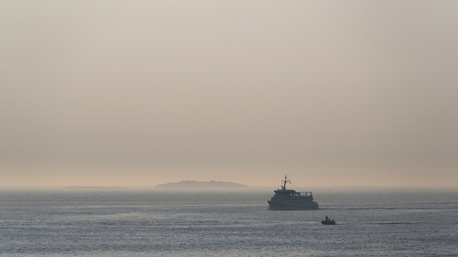 A small ship on a misty grey open sea with a faint island on the horizon
