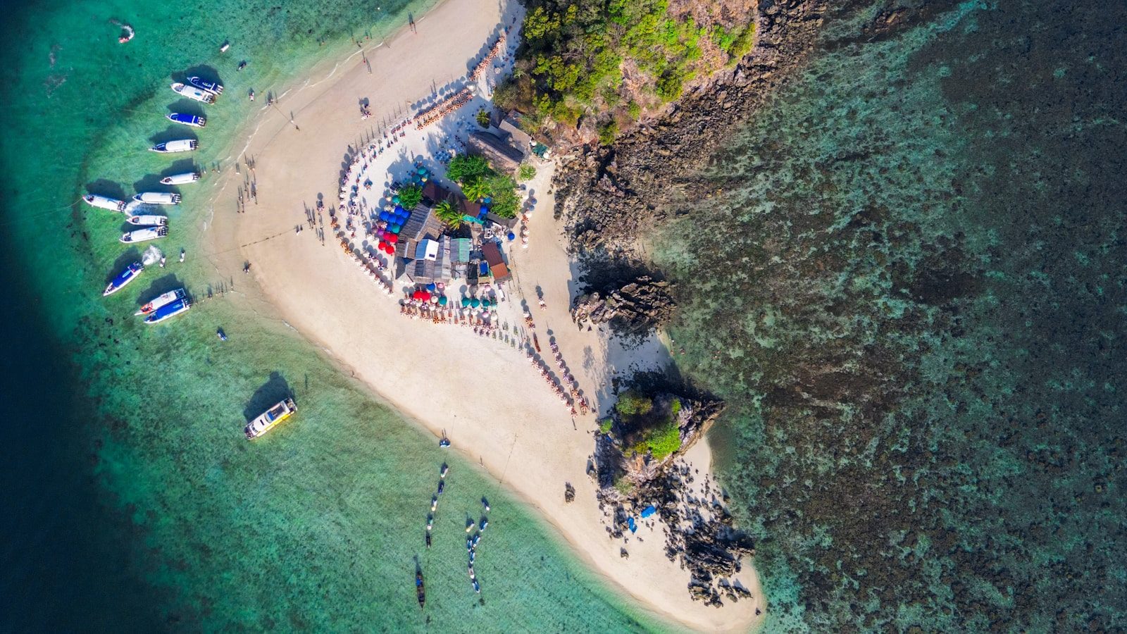 Aerial view of a small island ringed by a pale beach and turquoise water in an open sea