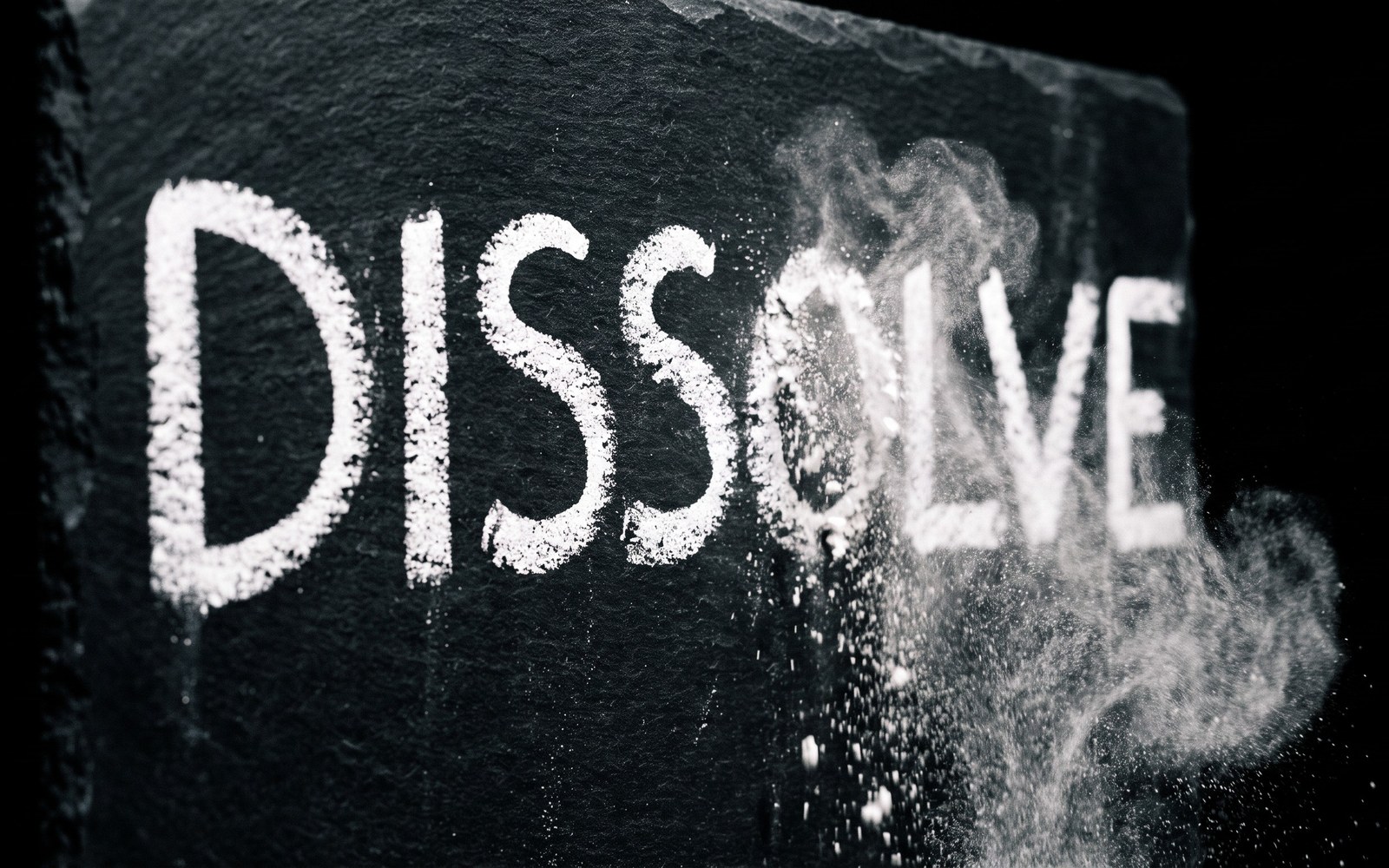 A word written in white chalk on a dark blackboard, the last few letters trailing off into fine chalk dust before completion