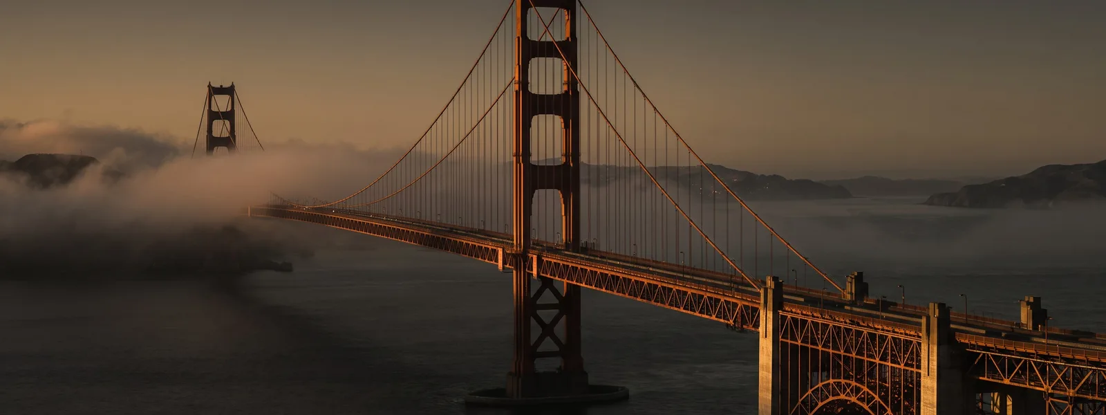 The Golden Gate Bridge at dawn, fog rolling through the towers