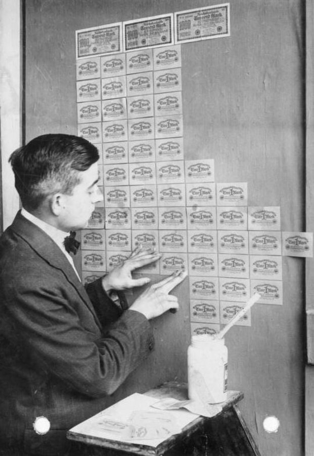 A German woman pasting worthless banknotes to a wall as wallpaper during the 1923 hyperinflation.