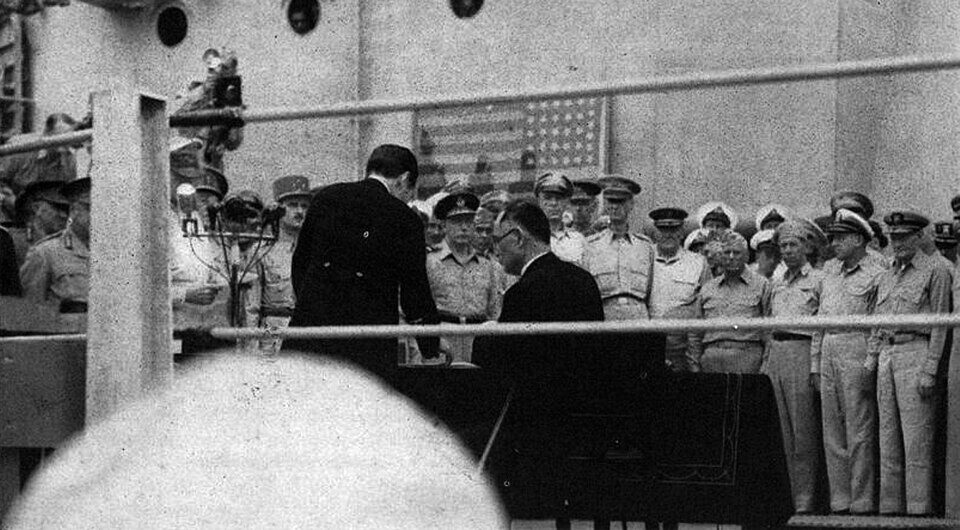 Japanese Foreign Minister Mamoru Shigemitsu signs the Instrument of Surrender aboard USS Missouri in Tokyo Bay, September 2, 1945, watched by General MacArthur and Allied officers.