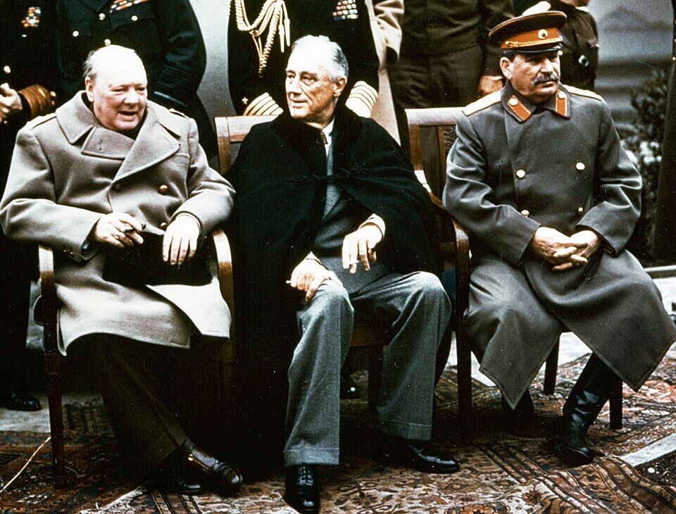 Churchill, Roosevelt, and Stalin seated together at the Yalta Conference, Livadia Palace, February 1945, with aides standing behind them.