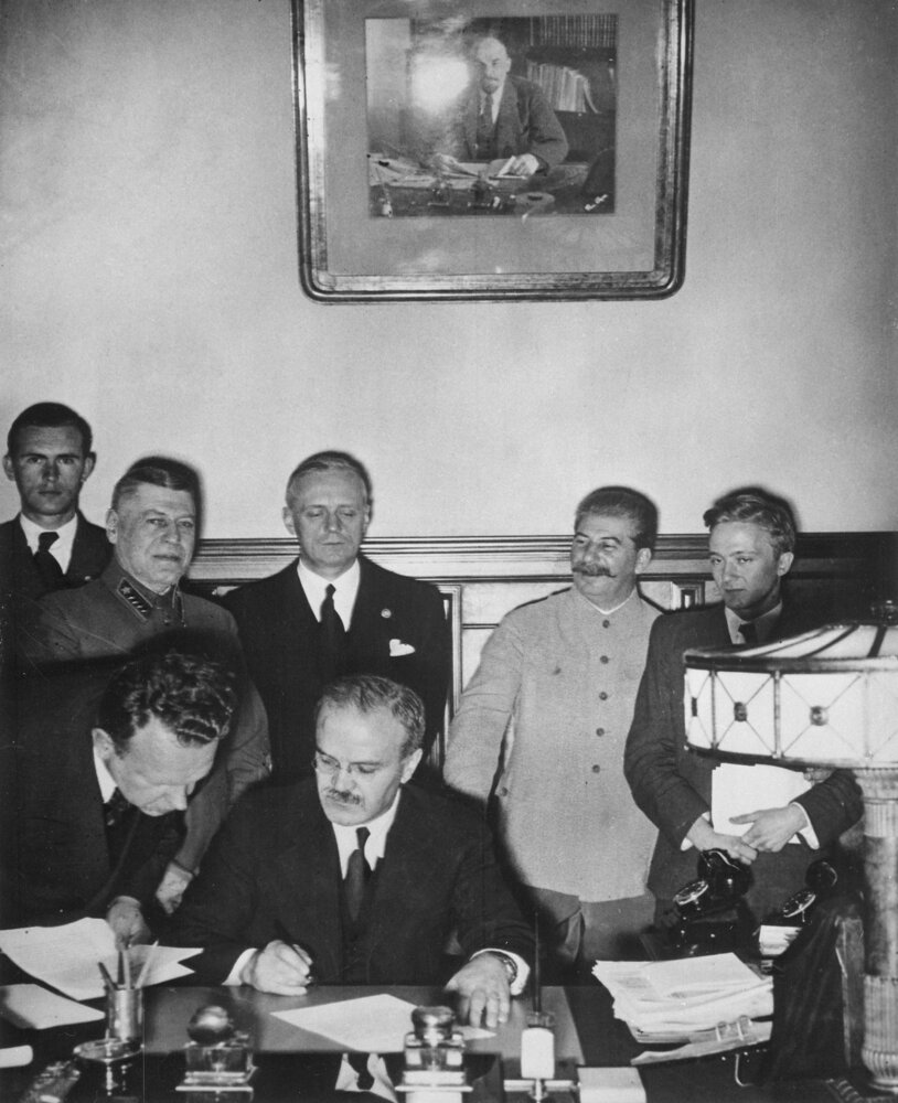 Soviet foreign minister Vyacheslav Molotov signing the Molotov-Ribbentrop Pact in the Kremlin, Moscow, in the early hours of August 24, 1939, with Joachim von Ribbentrop and Joseph Stalin standing behind him.